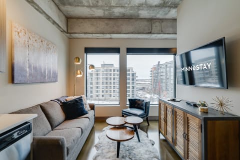 Stylish living room featuring a gray sofa, circular wooden coffee tables, and large windows with a view of surrounding buildings.