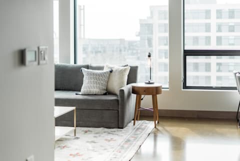 Modern living room with gray sofa, patterned pillow, wooden side table, and lamp by the window.