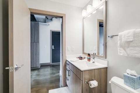 Modern bathroom with white countertops, wood cabinetry, and polished concrete floors.