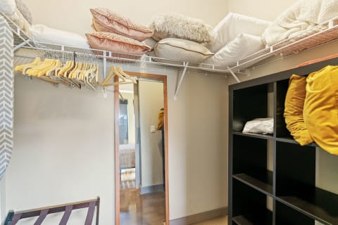 A cozy closet showing shelves with pillows, hangers, and a mirror reflection.