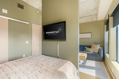 Interior view of a hotel room with a bed, TV, and a blue sofa.