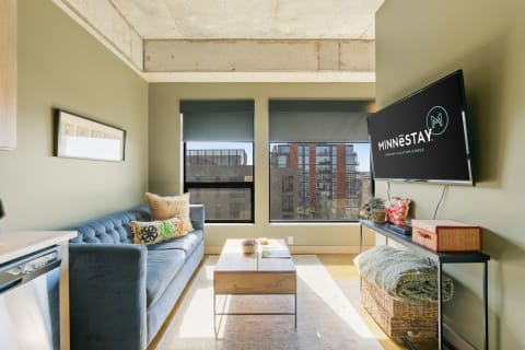 Modern living space with a blue sofa, wooden coffee table, and urban view through large windows.