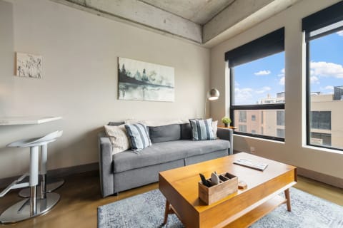 Modern living room featuring a gray sofa, artwork, large windows, and wooden coffee table.