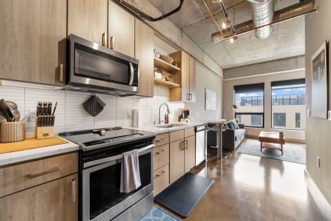 A modern kitchen and living area showcasing sleek cabinetry and a gray couch with large windows.