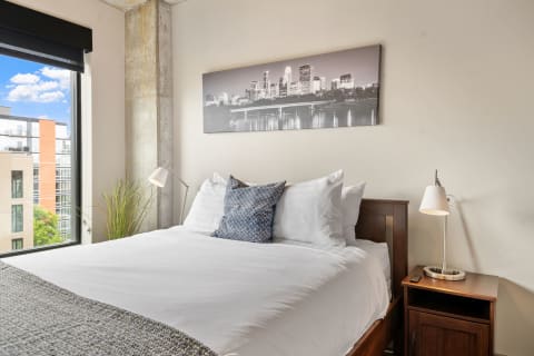 Modern bedroom with a plush bed, city skyline artwork, and bright window.