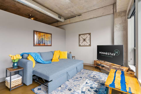 Contemporary living room with blue sectional sofa, yellow tulips, and forest artwork.