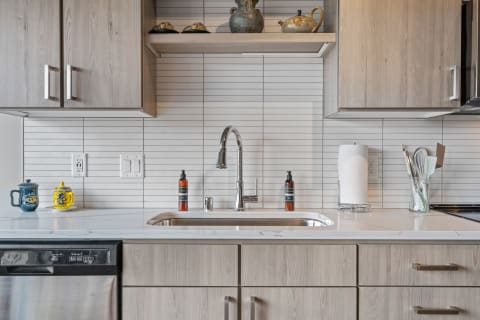 A contemporary kitchen sink with decorative items, modern faucet, and light wood cabinetry.