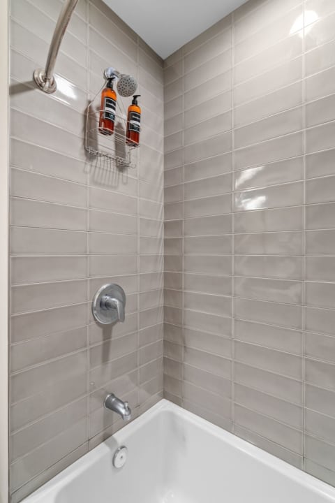 Contemporary shower stall with gray tiles and shampoo bottles.