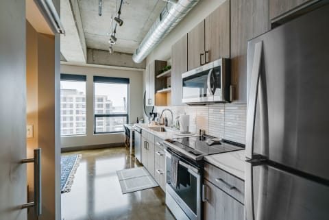 A sleek kitchen with stainless steel appliances and large city-view windows.