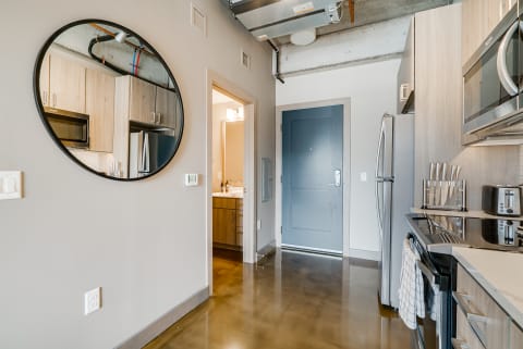Contemporary kitchen space with round mirror, gray door, and polished concrete flooring.