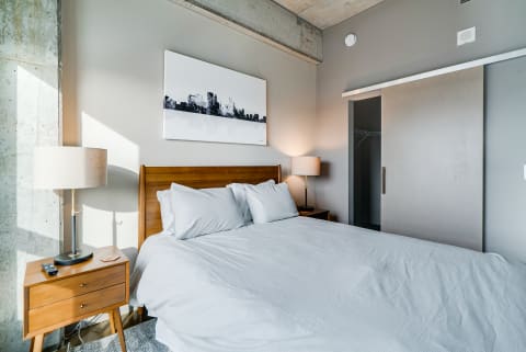 A neatly arranged modern bedroom with a gray color scheme and a city skyline painting.