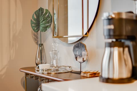 Stylish kitchen countertop with a coffee maker, glass decanter, monstera leaf, and decorative elements.