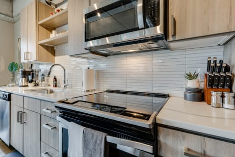 Modern kitchen featuring stainless steel appliances, light wood cabinets, and a white stone countertop.
