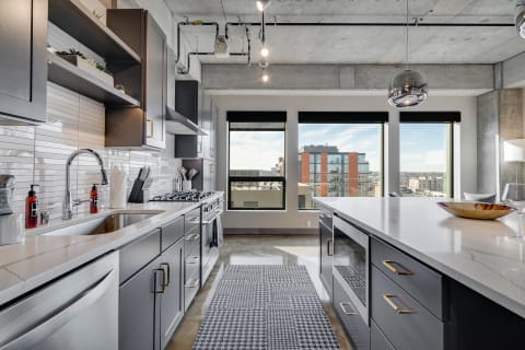 Modern kitchen featuring dark cabinets, marble countertops, and large windows with city views.