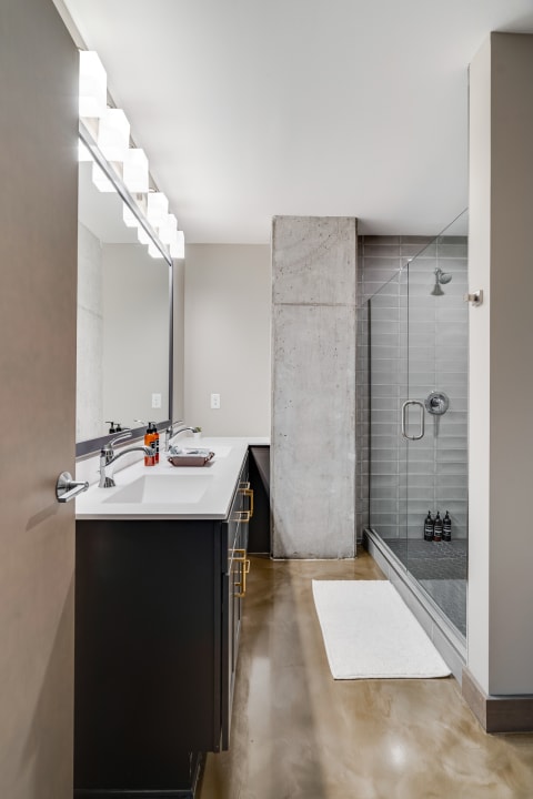 Modern bathroom featuring a dark vanity, bright lighting, and a glass shower enclosure.
