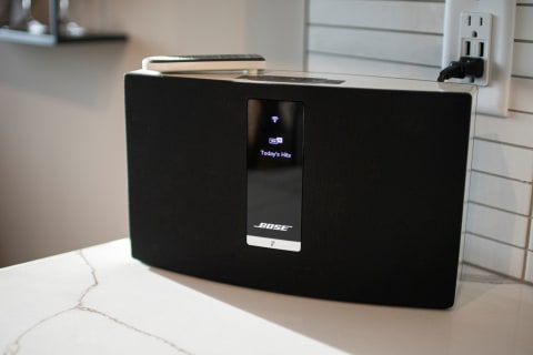 Bose speaker on a marble countertop showing a digital display of music streaming.