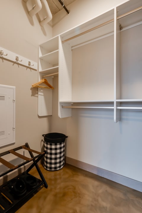Contemporary closet interior with white shelves, a black and white laundry basket, and a folding stool on polished concrete flooring.