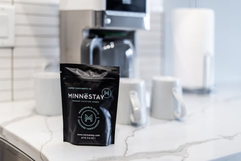 A black coffee bag from MINNēSTAY on a marble countertop in a contemporary kitchen.