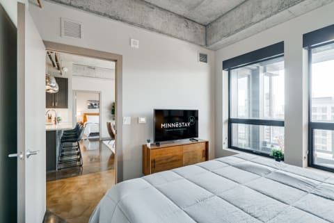 Modern bedroom with large windows and a flat-screen TV, showcasing an industrial interior design.