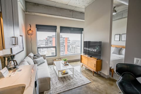 Modern studio apartment interior featuring a sofa, coffee table, and TV with city views.