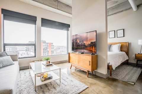 Modern studio living space with a sofa, coffee table, and a view of the city through large windows.