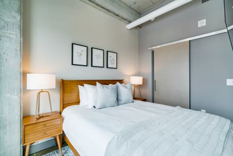 Modern bedroom with wooden bed, grey pillows, and botanical artwork on walls.