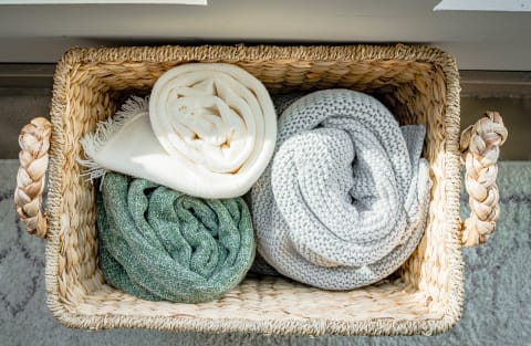 Woven basket containing neatly rolled blankets in cream, green, and gray.