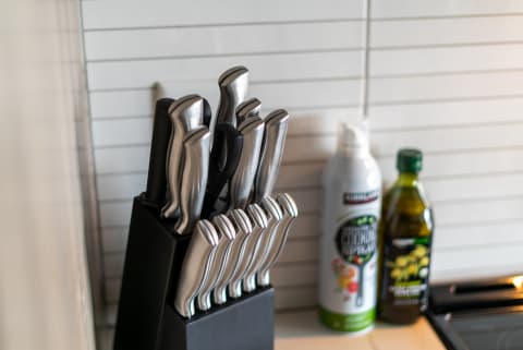 Knife block filled with modern kitchen knives next to olive oil and cooking spray bottles.
