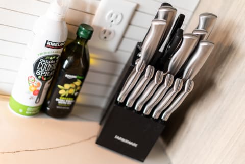 Knife block with stainless steel knives next to olive oil and cooking spray in a kitchen.