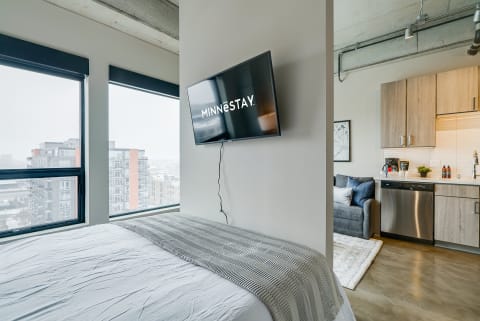 Modern studio apartment featuring a bed, TV, and kitchen area with a winter view outside.