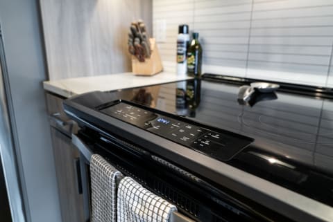 Close-up of a contemporary black glass cooktop stove with digital display and kitchen utensils.