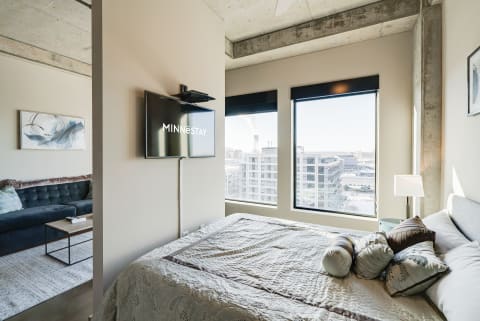 Stylish bedroom corner with a bed, decorative pillows, city view, and mounted television.