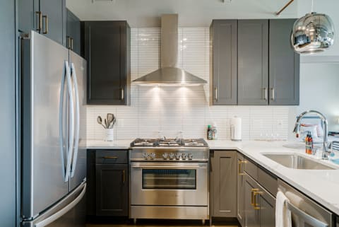 Modern kitchen with grey cabinets, stainless steel appliances, and white countertop.