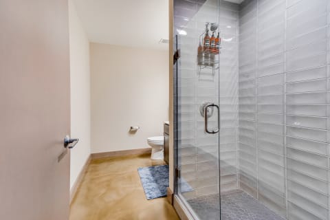 A contemporary bathroom with a glass shower, toilet, and a blue bath mat on a polished concrete floor.