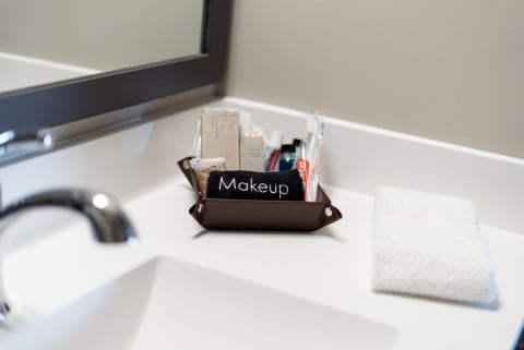 A brown tray with makeup products labeled 'Makeup' next to a folded white washcloth on a bathroom counter.