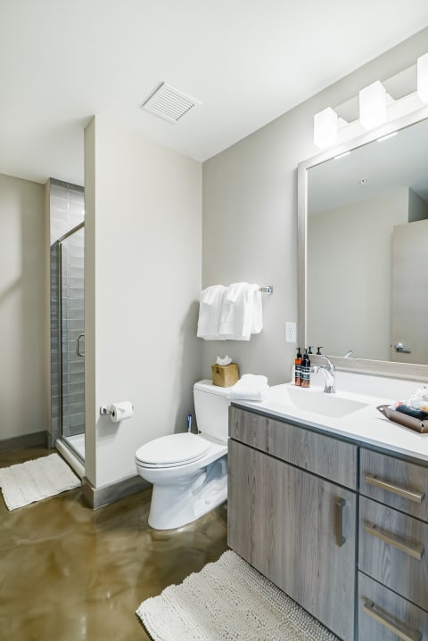 A contemporary bathroom with a glass shower, white sanity ware, and a grey vanity with neatly organized toiletries.