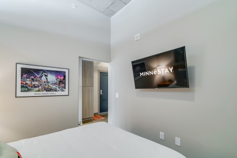 Modern hotel room with a bed, artwork, and a TV displaying the 'MINNESTAY' logo.