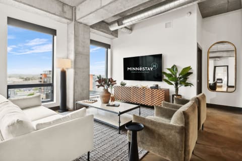 A bright living room featuring a white sofa, green armchairs, a marble coffee table, and a TV mounted on the wall.