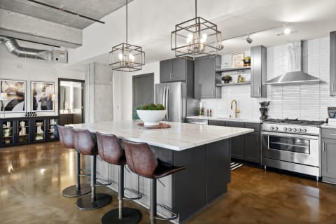 Modern kitchen featuring a marble countertop island, dark cabinetry, and stylish lighting.