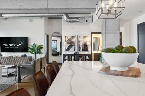 A contemporary kitchen and living space with a marble countertop, leather stools, and modern decor.
