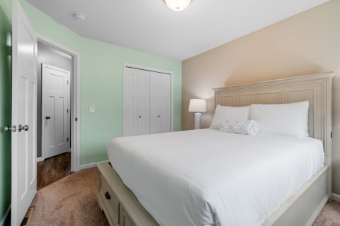 A spacious bedroom with a white bed, mint green and beige walls, and closet doors.