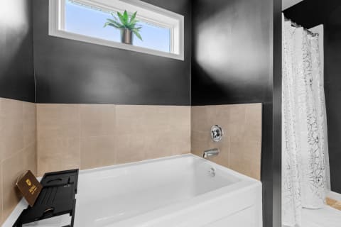 Modern bathroom with a white bathtub, black and beige tiles, and a green plant by the window.