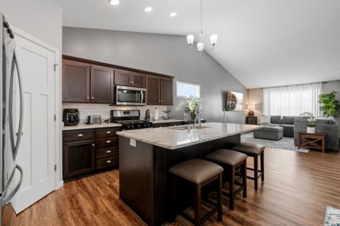 Modern kitchen with dark wood cabinets and light granite countertops adjacent to a cozy living area.