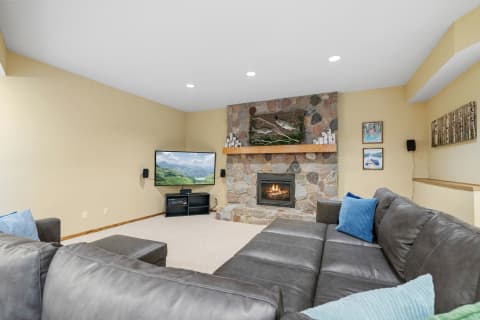Living room with a stone fireplace, sectional sofa, and mounted television.