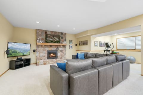 A stylish basement living room with a stone fireplace, sectional sofa, and fitness area.
