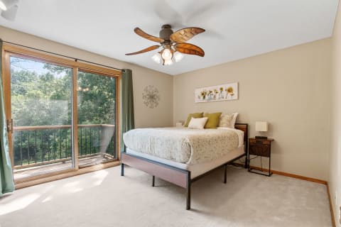A well-lit bedroom featuring a queen bed, green curtains, and a balcony view.