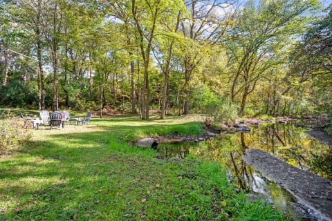 A tranquil outdoor scene with chairs by a stream surrounded by trees.