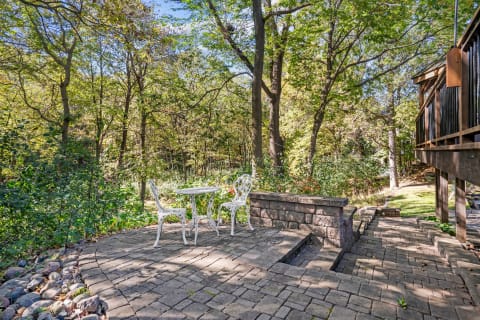 Outdoor patio with a round table and two white chairs in a green natural setting.