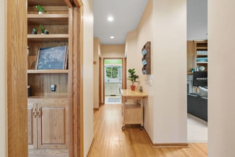 A wooden hallway with shelves, a small table, and a doorway to a bright room.