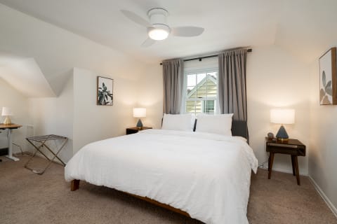 A cozy bedroom with a large white bed, nightstands, and gray curtains.